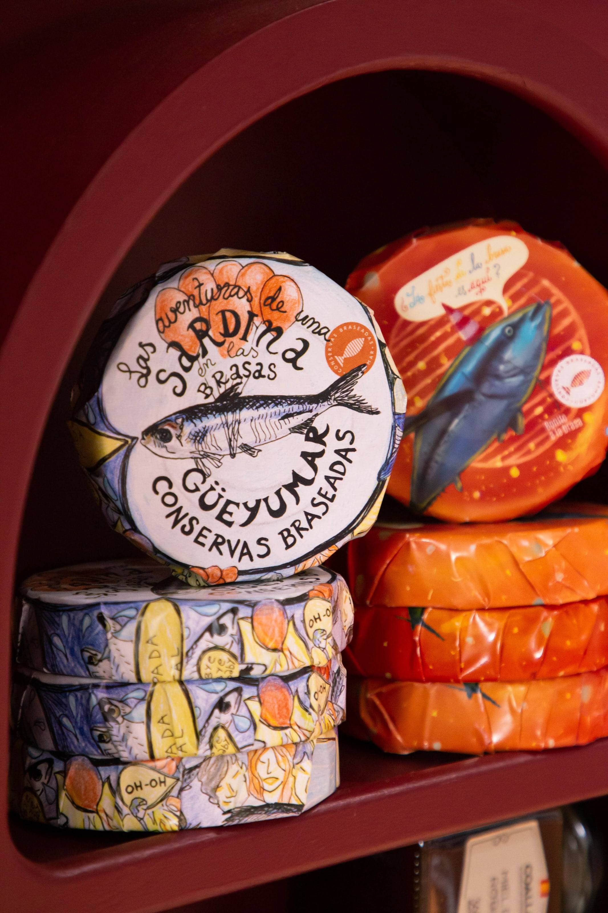 Latas ilustradas de conservas de sardina y bonito en una hornacina granate de La Prudencia.