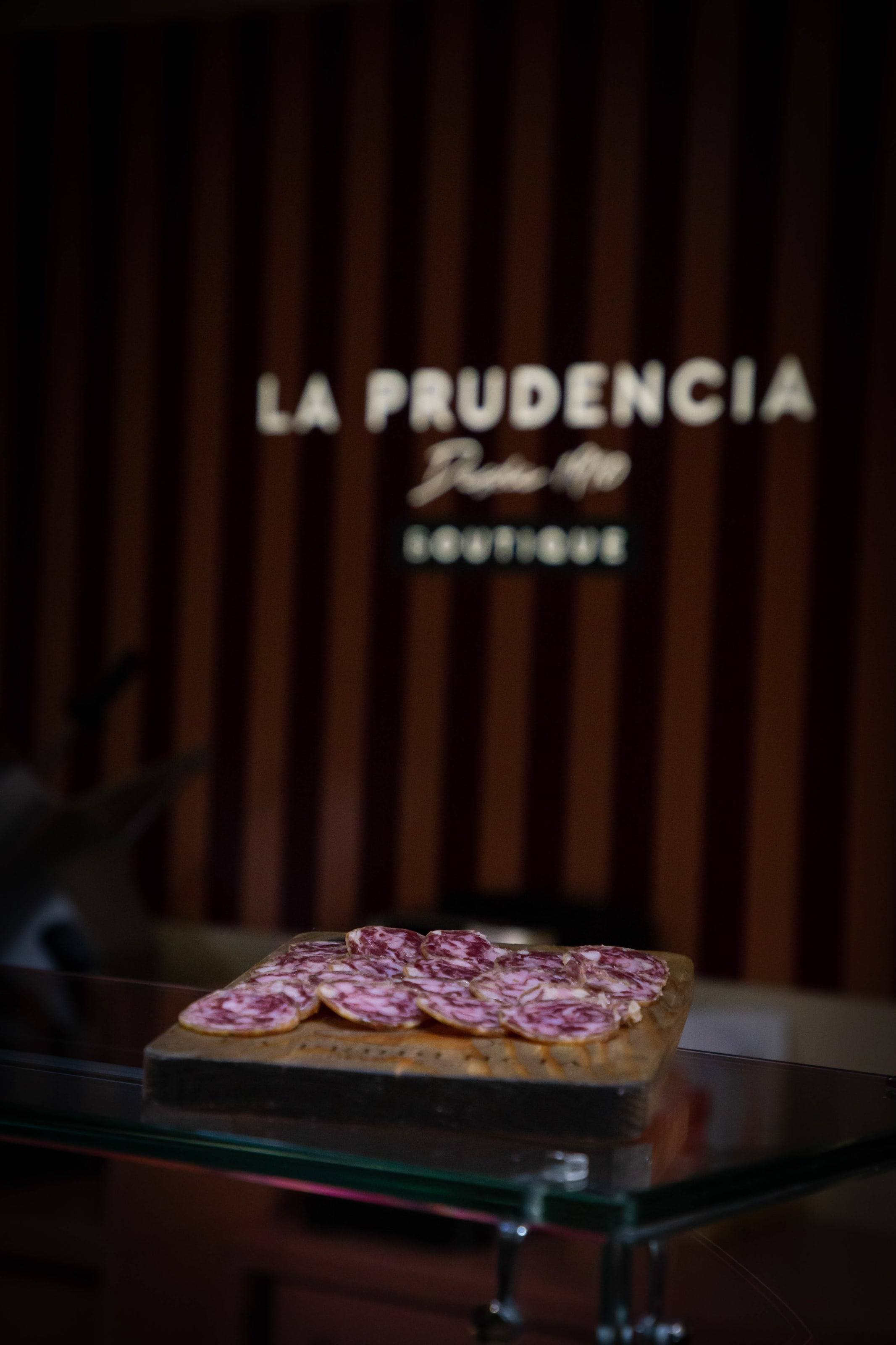 Rótulo de La Prudencia Boutique con una tabla de embutido en primer plano