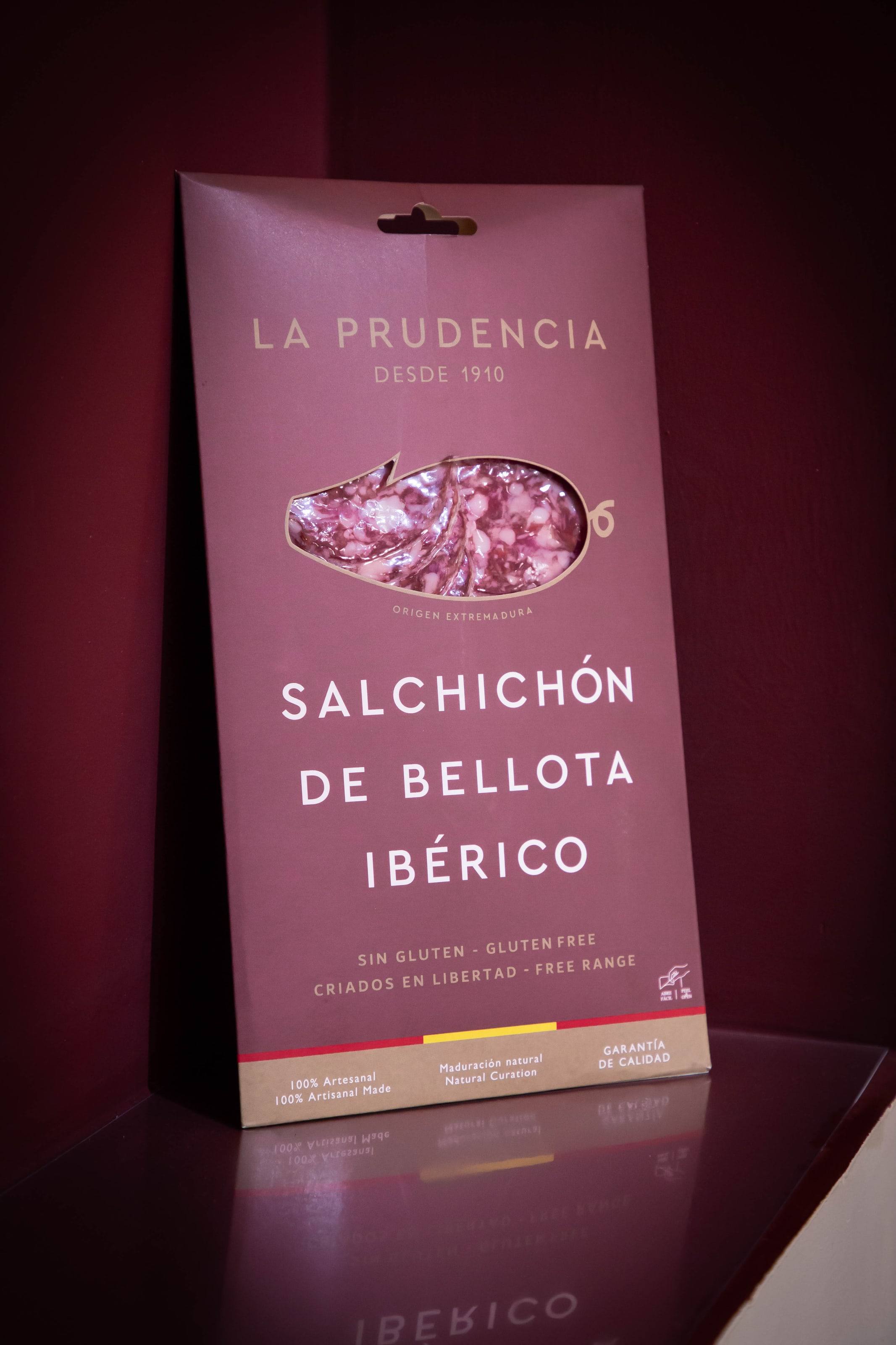 Paquete de salchichón de bellota ibérico de La Prudencia sobre fondo granate.