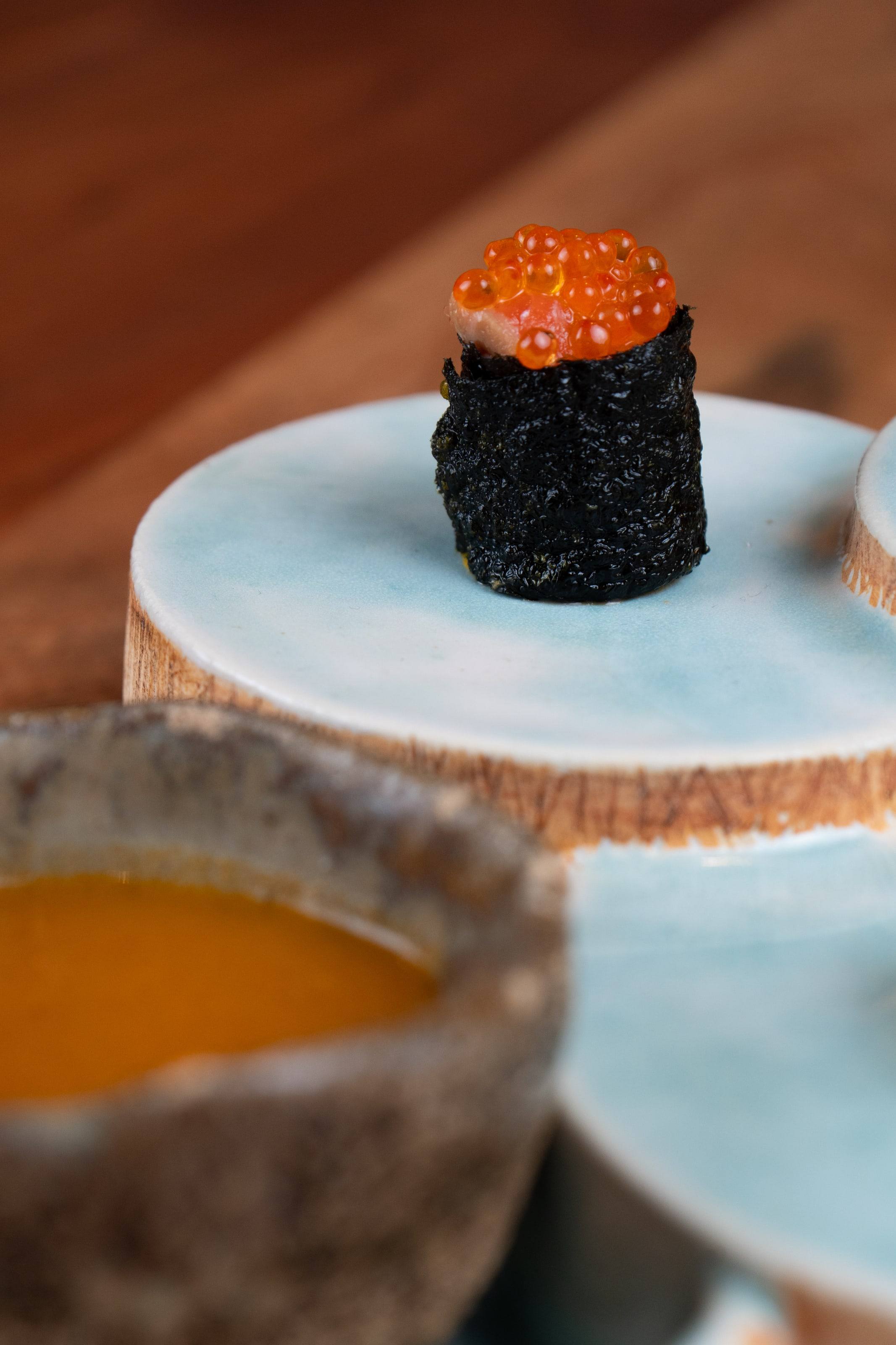 Bocado de arroz negro coronado con huevas de salmón sobre un plato de cerámica claro.