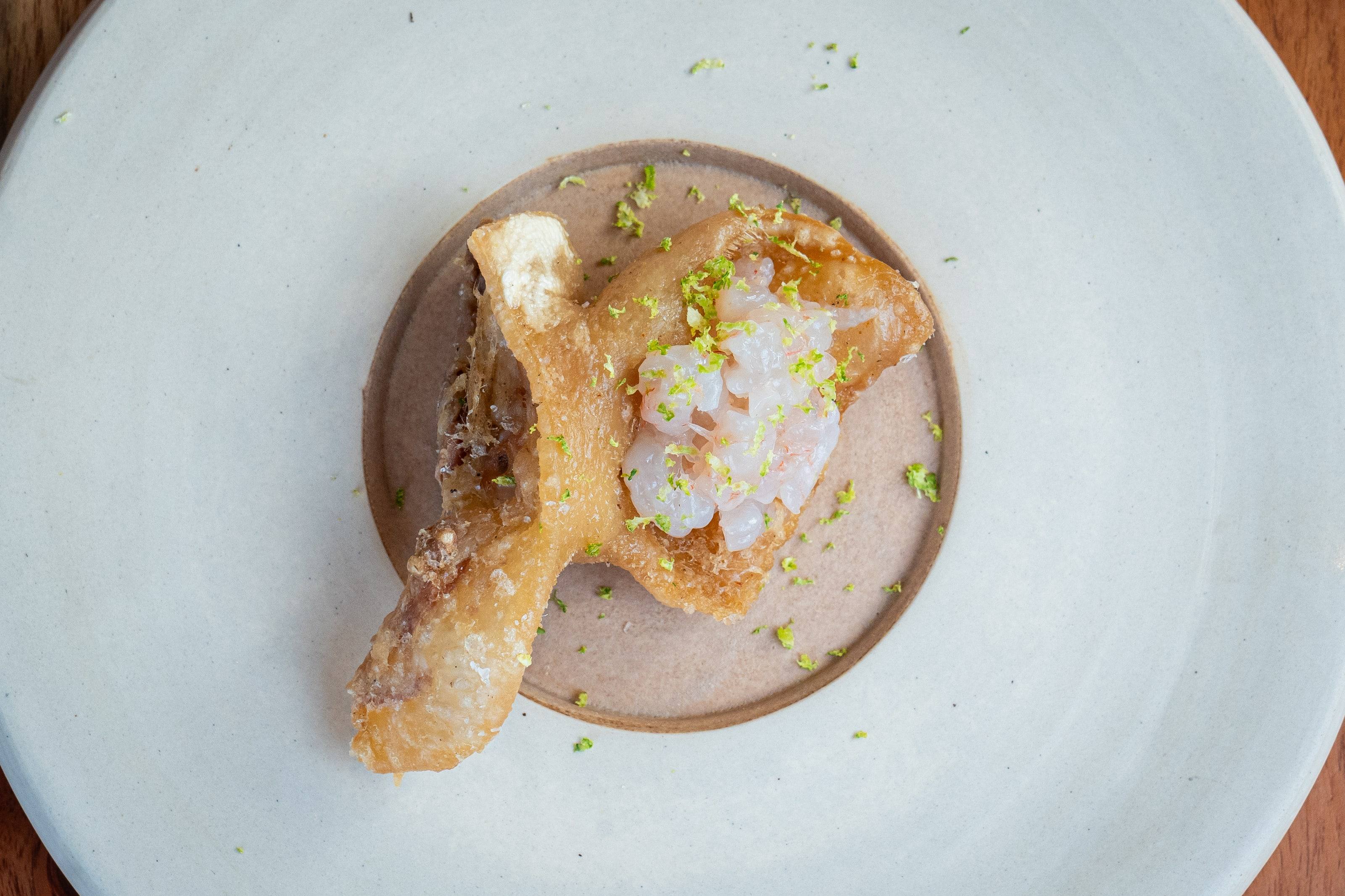 Crujiente de cerdo con tartar y ralladura de lima sobre un plato de cerámica.