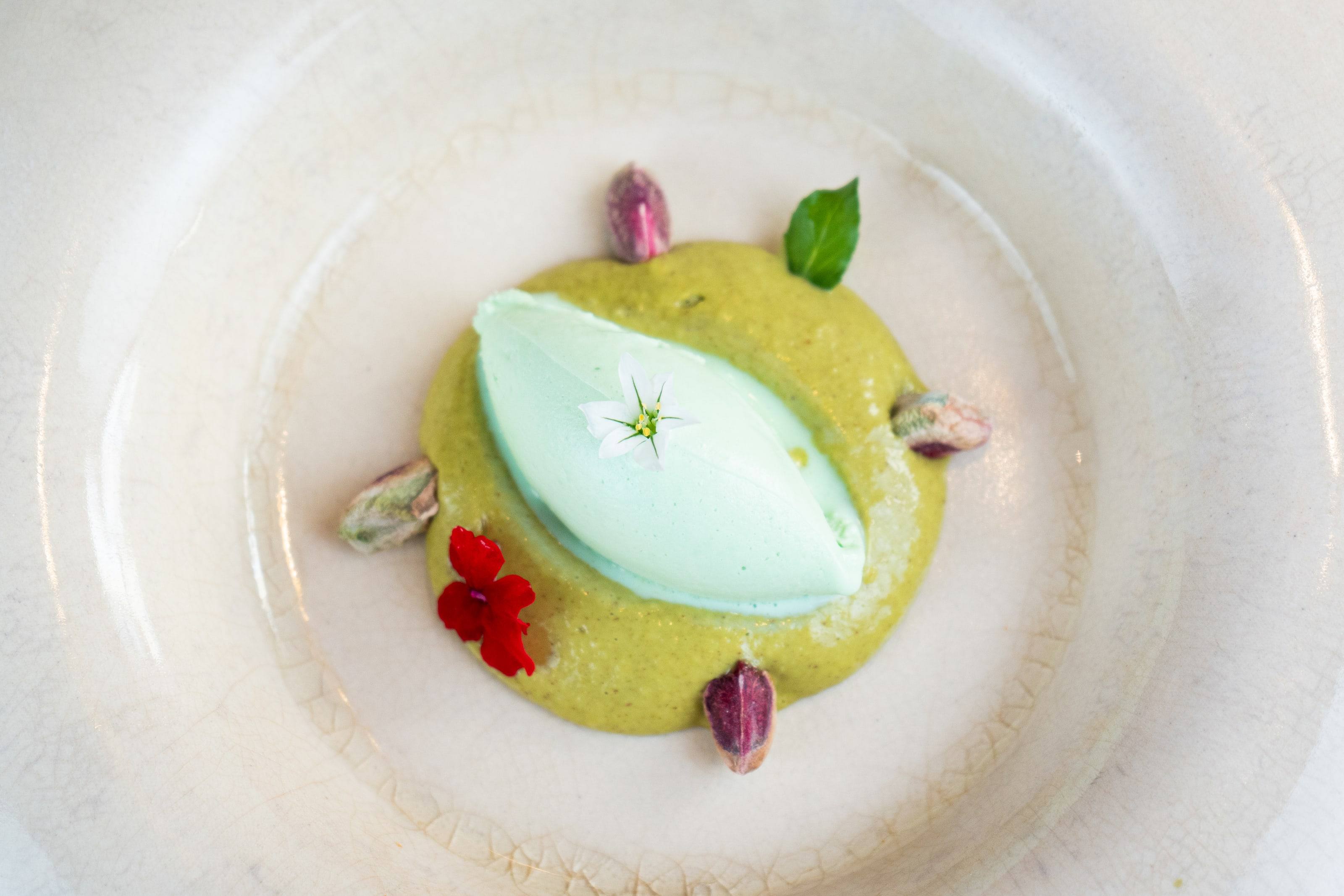 Helado verde sobre crema de pistacho con pistachos y pétalos rojos, un postre de Borona Bistró.