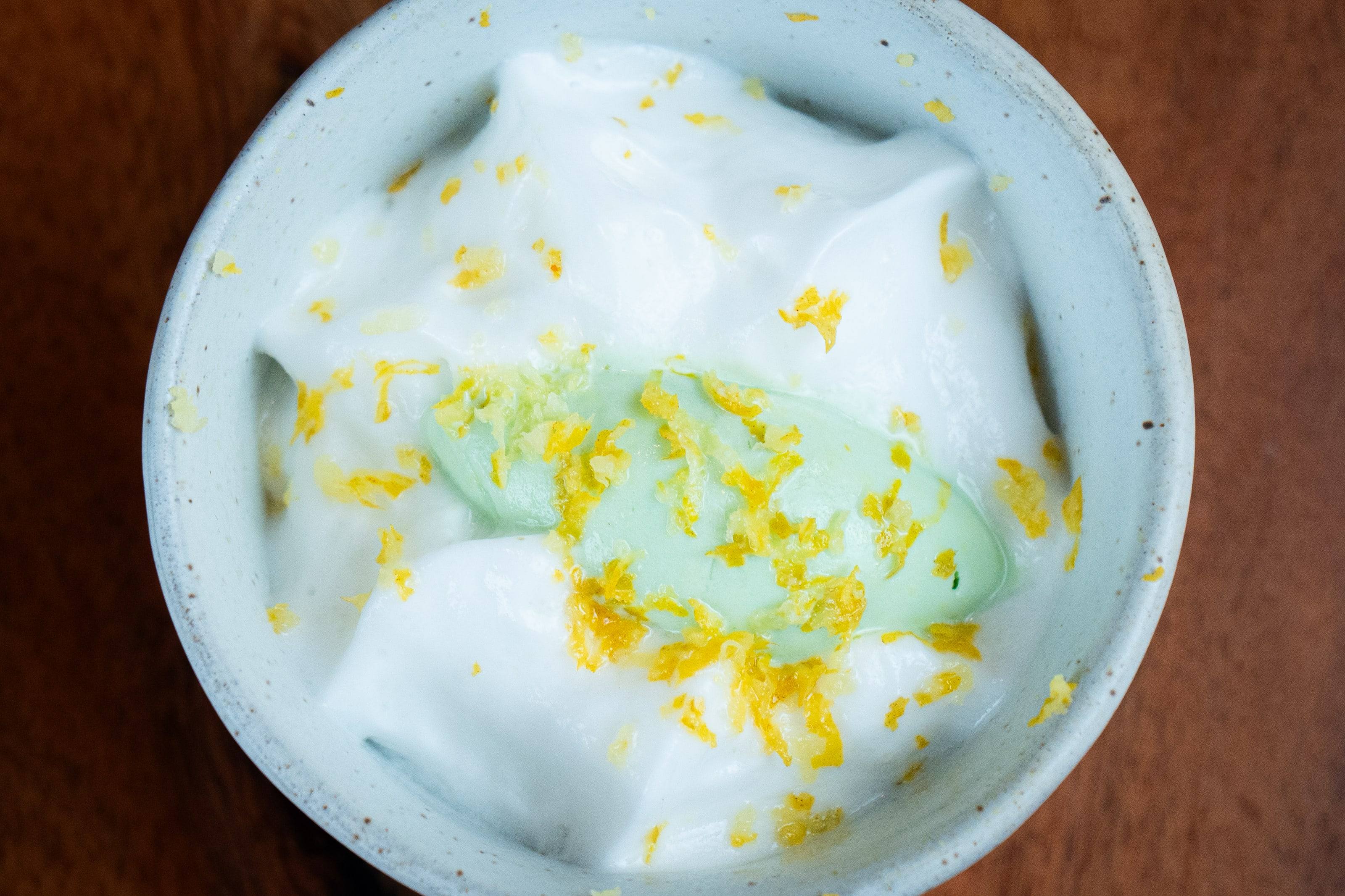 Detalle de un postre de espuma blanca con ralladura de limón y crema verde.