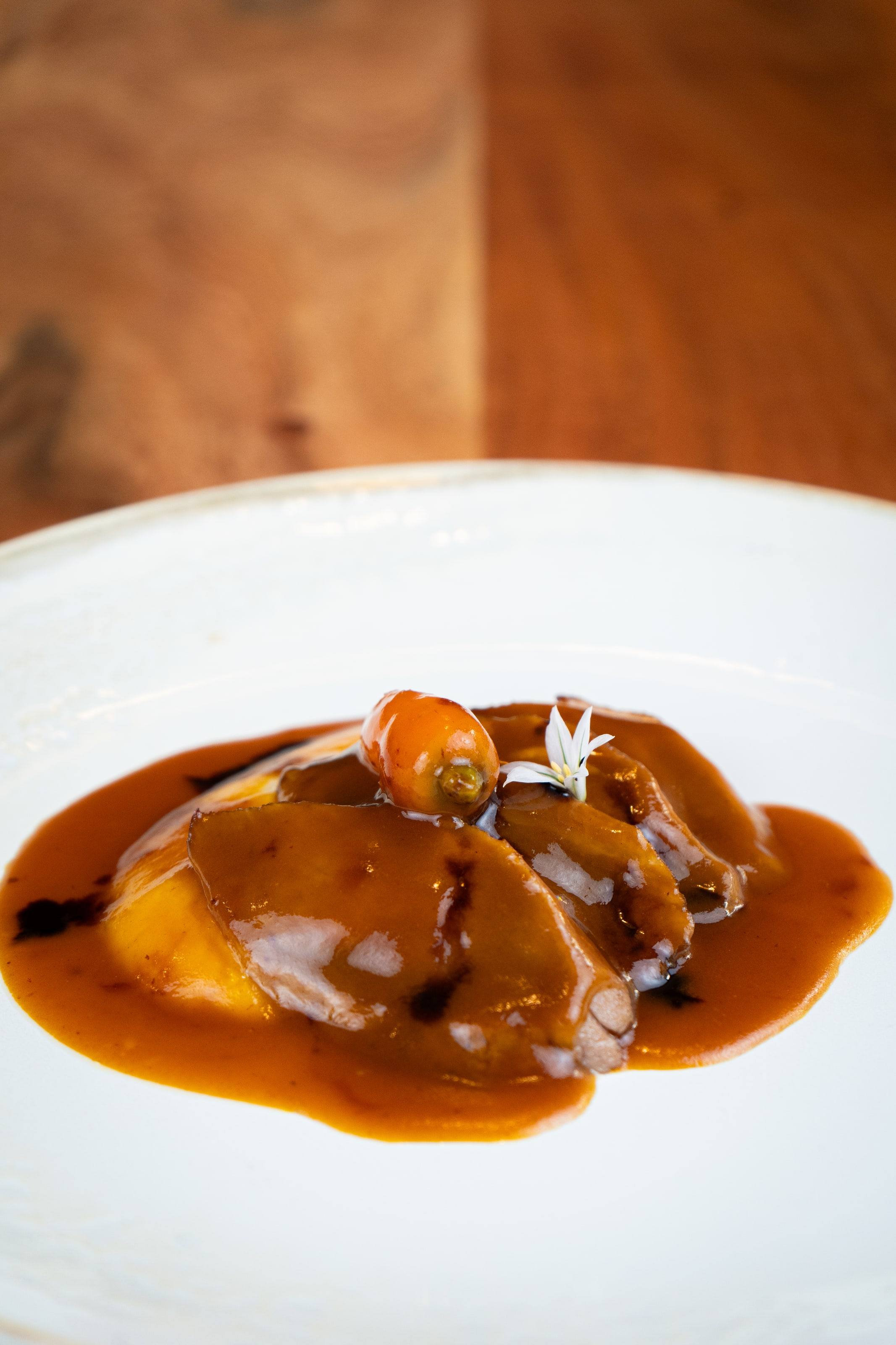 Carne guisada con salsa brillante y zanahoria glaseada sobre un plato blanco.