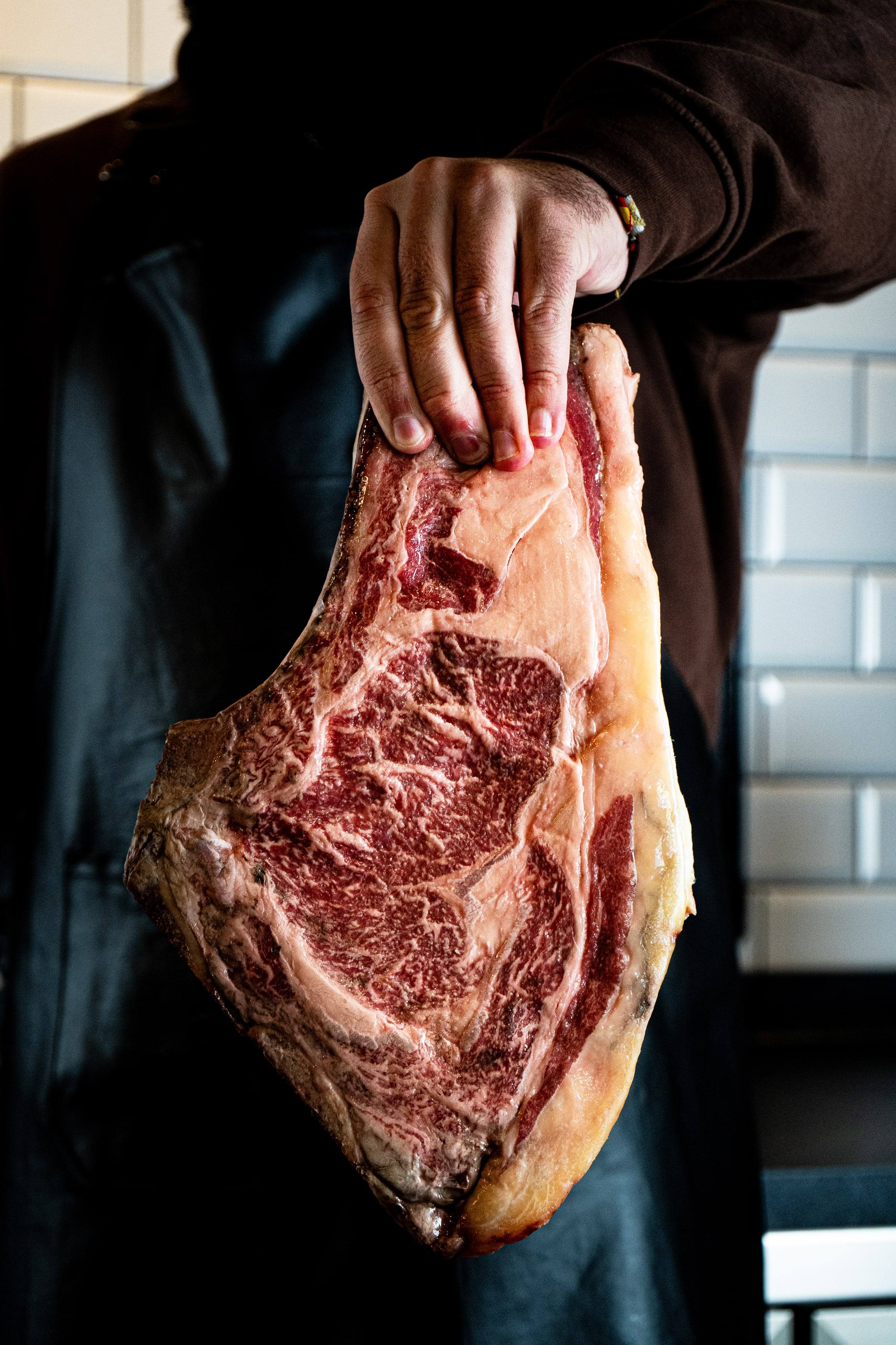Mano sosteniendo un chuletón madurado de vaca con mucha grasa infiltrada.