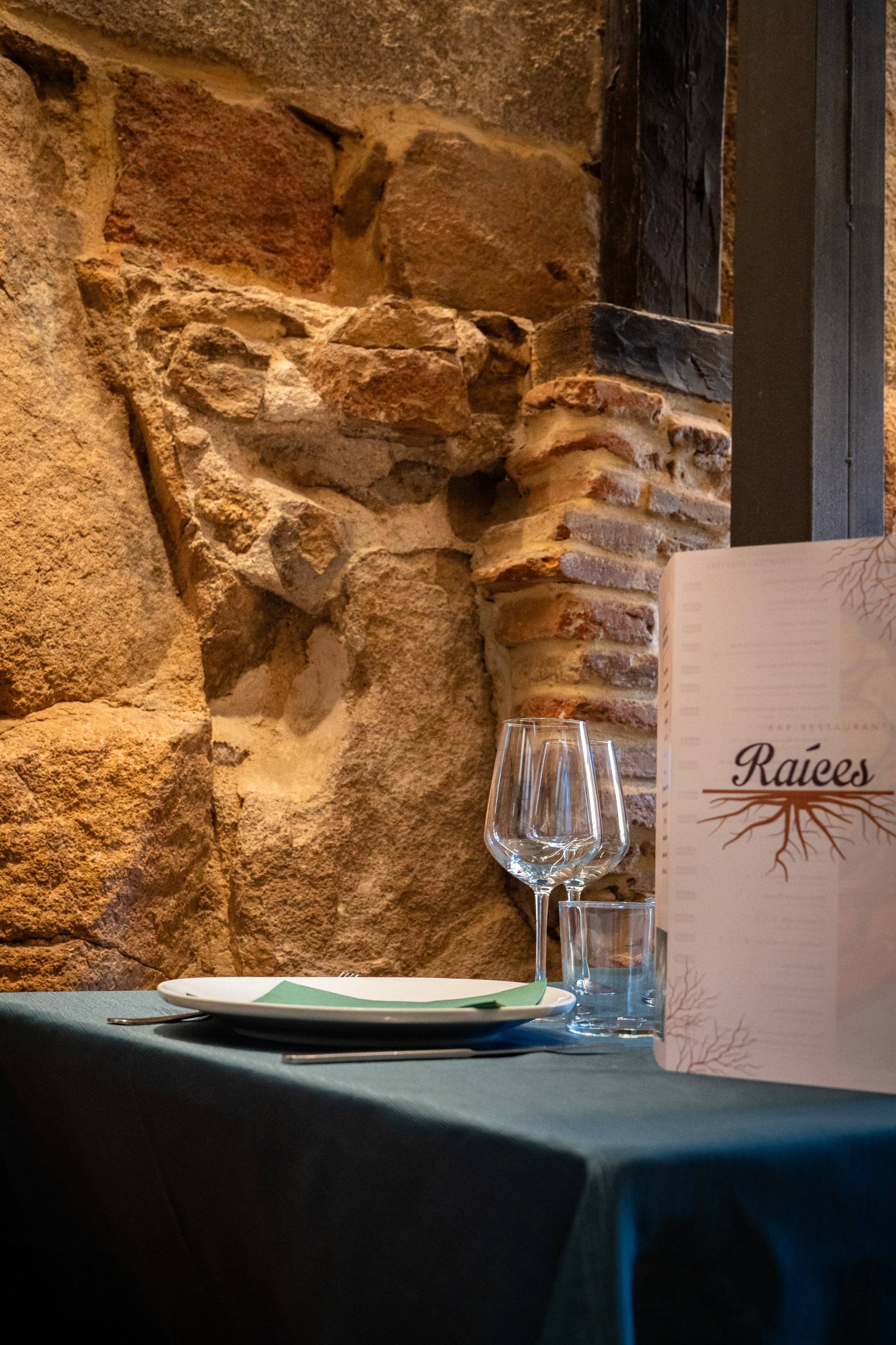 La carta del restaurante Raíces sobre una mesa junto a una pared de piedra.