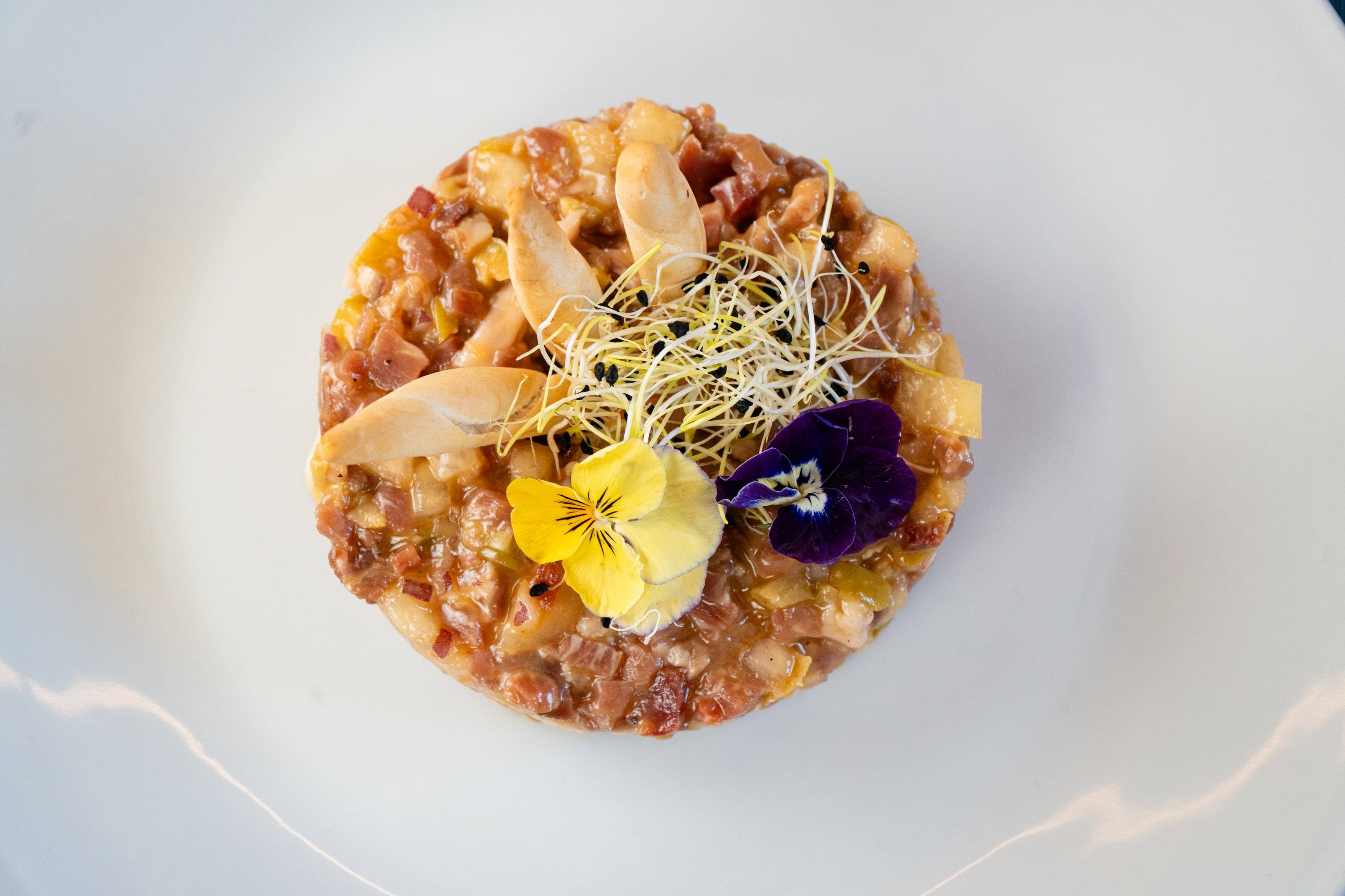 Tartar con pensamientos amarillos y morados y brotes, plato del restaurante Raíces.