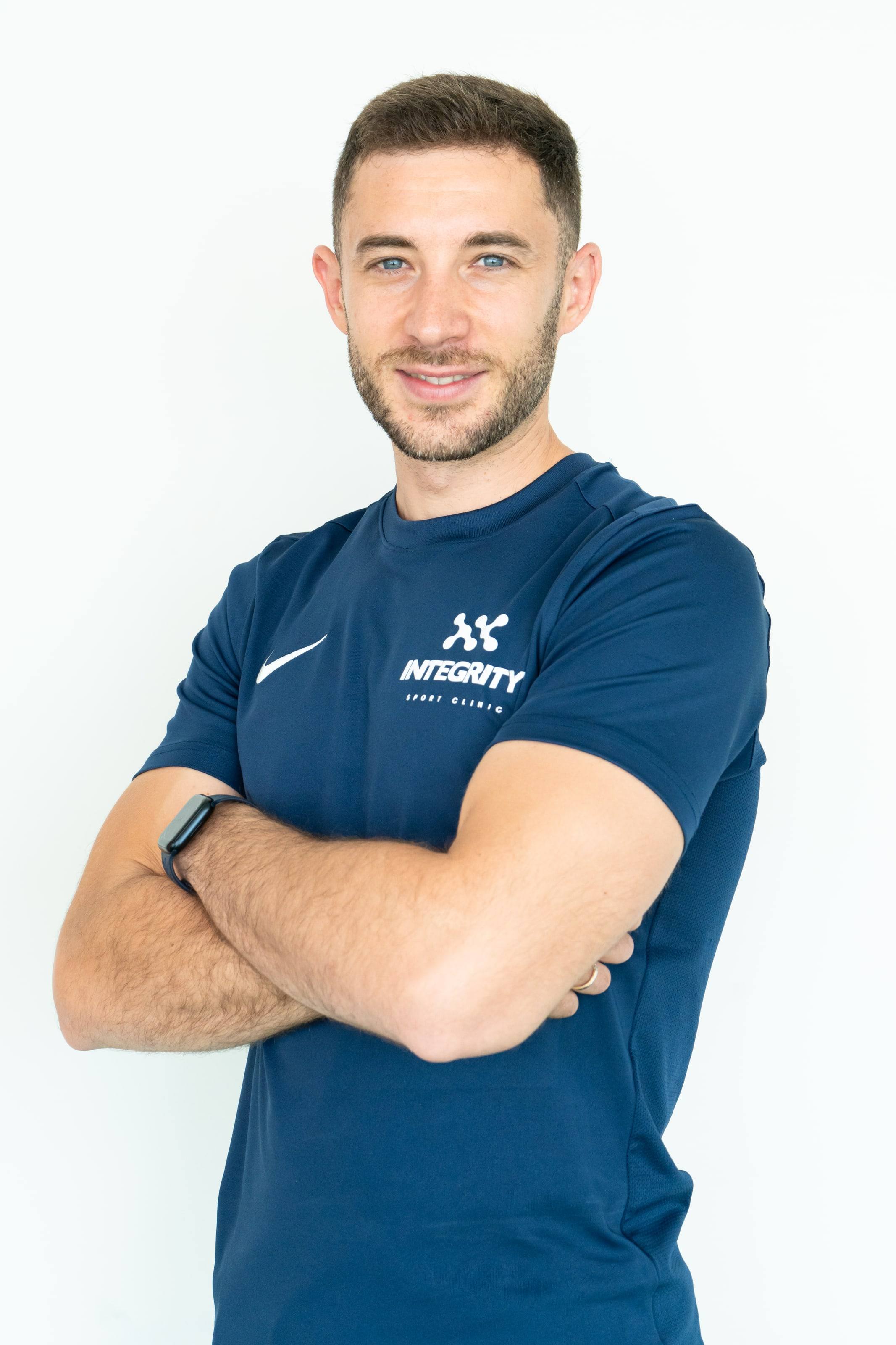 Fisioterapeuta de Integrity Sport Clinic con los brazos cruzados, retrato sobre fondo blanco.